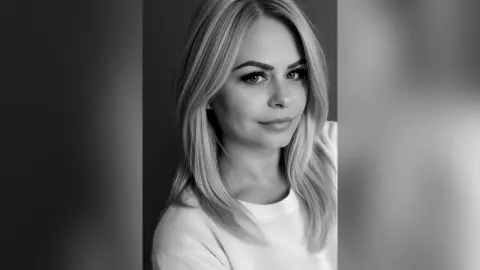 Portrait of a smiling blonde woman in a white top against a minimalist studio background in black and white.