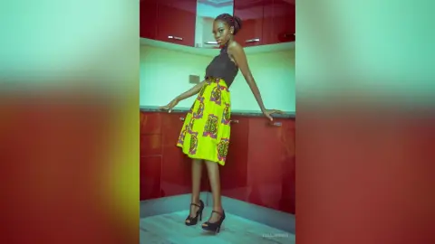 Young woman in a black halter top and vibrant yellow patterned skirt posing in a modern kitchen.