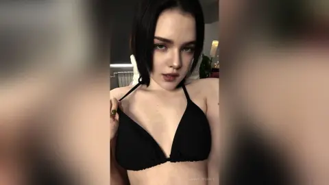Young woman with dark hair wearing a black bikini top in a moody indoor setting.