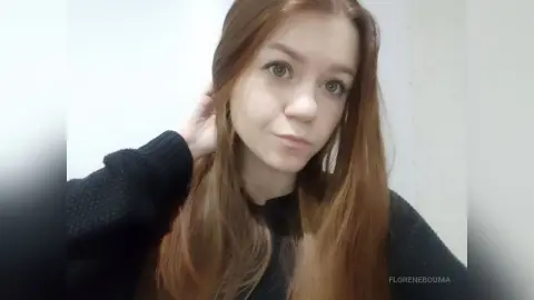 Redheaded woman in a black knit sweater posing against a white wall in a soft, natural light mood.