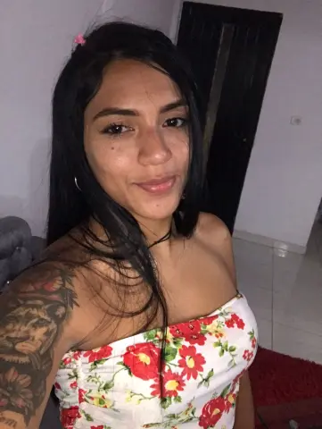 SusanaGlace smiles while wearing a white strapless floral top, showing off her long black hair and large shoulder tattoo.