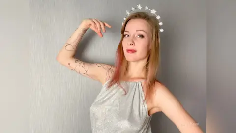 Smiling woman in a sparkly silver halter top wearing a star headband against a grey background.