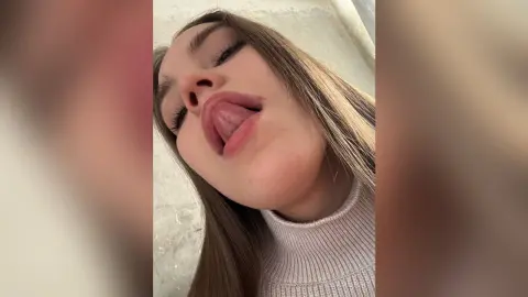 TessaMilton looks into the camera with her tongue out, wearing a beige ribbed turtleneck sweater.