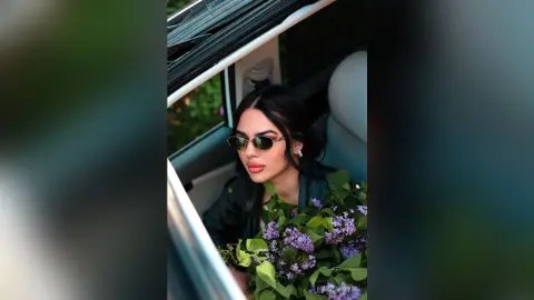 Stylish woman with sunglasses holding a large lilac bouquet sitting in a car for a romantic spring mood.