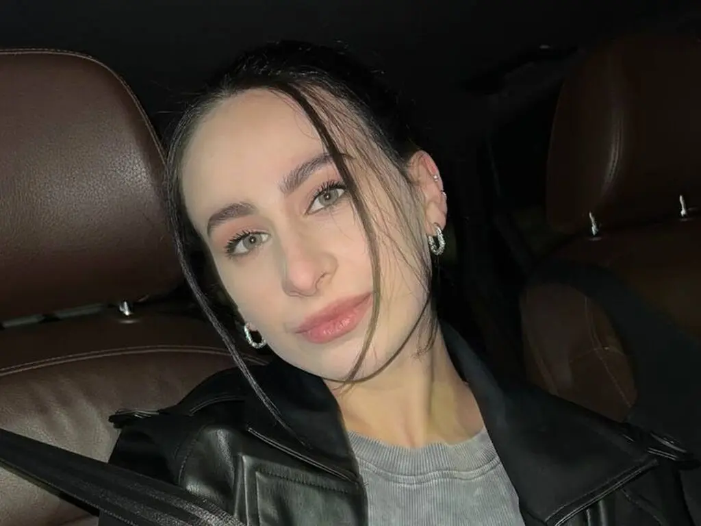 Young woman with dark hair and hoop earrings wearing a black leather jacket sitting in a car at night.