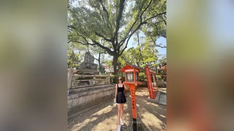 Stylish woman in a black dress standing by traditional red lanterns at a serene Japanese shrine garden.
