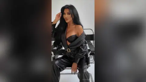 Glamorous woman in a chic black leather outfit posing confidently in a modern studio setting.