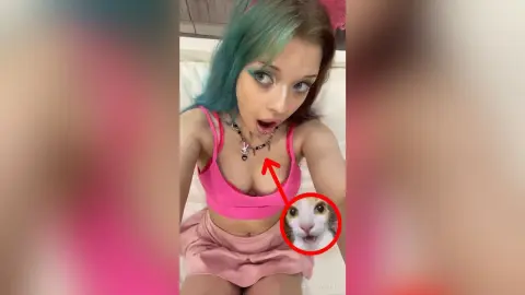 Young woman with blue hair in a pink outfit and necklace looking surprised in a bedroom setting.