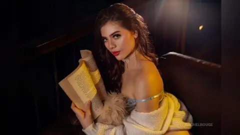 Elegant woman in a white off-the-shoulder outfit reading a book in moody, warm indoor lighting.