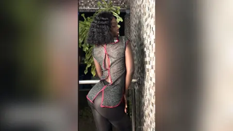 Stylish woman in a sparkly grey tunic and black leggings posing by a textured stone wall in natural light.