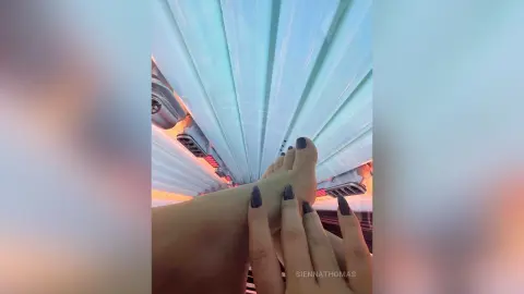 Close-up of feet with dark nail polish relaxing under bright blue spa lighting in a tranquil wellness setting.