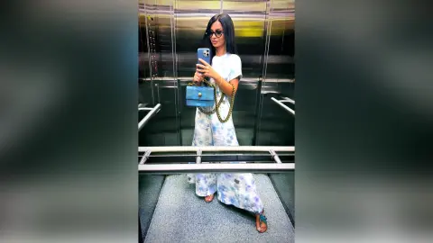 Stylish woman in blue tie-dye outfit and sunglasses taking a mirror selfie in a modern elevator.
