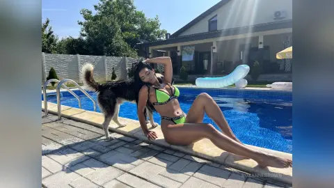 Young woman in a green bikini relaxing by a sunny backyard swimming pool with her dog.