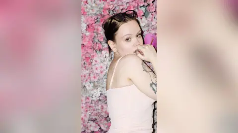 Young woman in a pink tank top posing against a romantic floral background with a soft, dreamy mood.