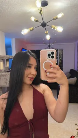 Smiling young woman in a burgundy halter top taking a mirror selfie in a cozy living room.