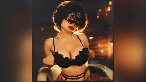 Glamorous woman in black lace lingerie and a sparkling masquerade mask posing in warm, moody lighting.