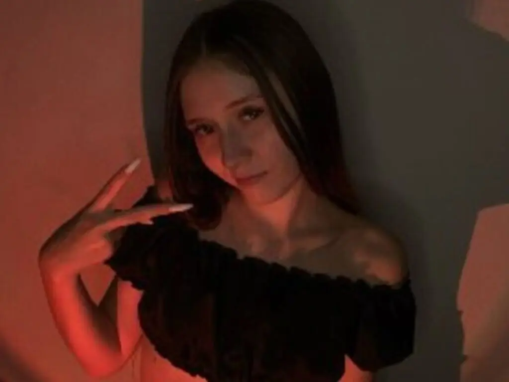 Young woman in a black off-the-shoulder top posing in moody, warm red lighting.