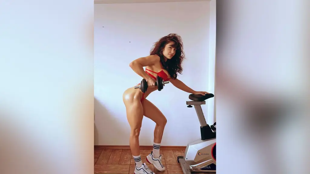 Athletic woman in a black bodysuit wearing red boxing gloves posing confidently against a white wall.