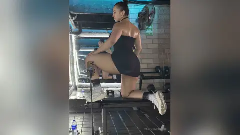 Curvy woman in black workout bodysuit performing squats on a gym bench during an intense fitness session.