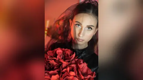 Moody portrait of a woman in a black veil holding a large bouquet of deep red roses.