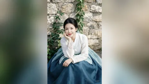 KimFu — KimFu sits in front of a stone wall wearing a traditional white and blue hanbok.