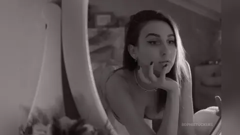 Thoughtful young woman in a white strapless dress posing in a bright, minimalist room in black and white.