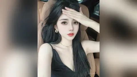 AgelaHui poses in a car seat wearing a black tank top, touching her long black hair with one hand.