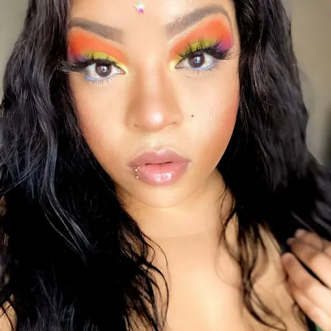 Woman with colorful rainbow eyeshadow and long wavy black hair posing for a vibrant beauty portrait.