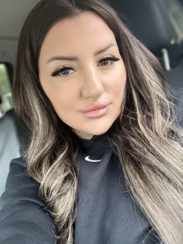 Beautiful woman with long wavy brunette hair wearing a black Nike top sitting in a car with a soft glow.