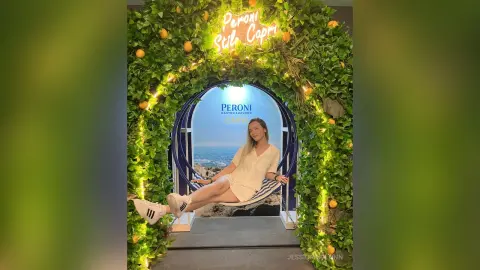 JessicaAidennn — Woman in white summer outfit relaxing in a hammock under a Peroni Capri floral archway on a sunny day.