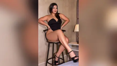 Confident woman in a black strapless bodysuit sitting on a stool in a modern minimalist room.