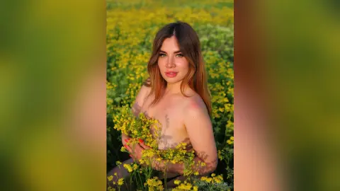 Beautiful woman with long hair posing in a yellow flower field during a golden hour sunset.