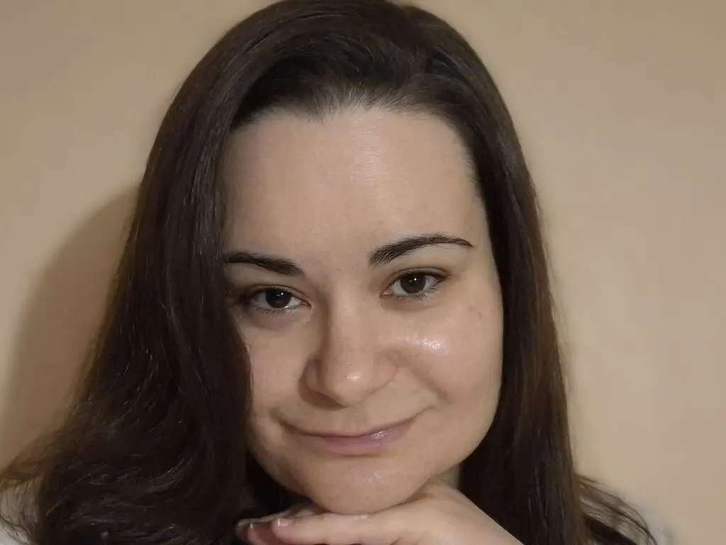 JustinaRay smiling at the camera with her long dark hair and hand under her chin.