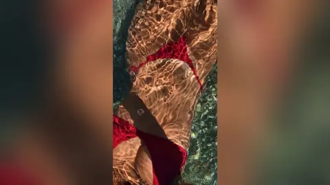 MarisaGrace wearing a red bikini while partially submerged in clear, rippling water.