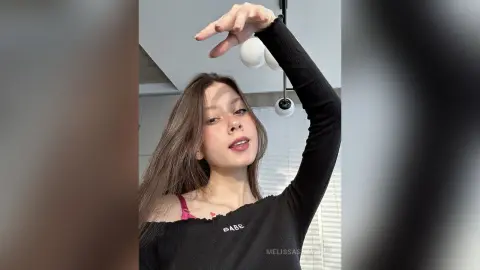Young woman in a black long-sleeve top posing indoors with a soft, natural aesthetic.
