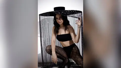 Stylish woman in a black strapless crop top and patterned tights posing under a shimmering sequin fringe canopy.