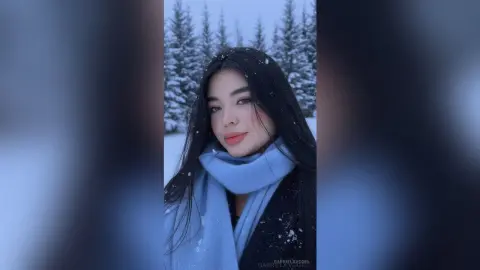 Young woman in a blue scarf smiling in a snowy winter forest setting.