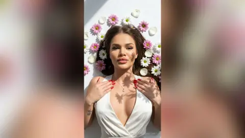 Beautiful woman in a white plunging dress lying amidst pink flowers for a dreamy, romantic portrait.