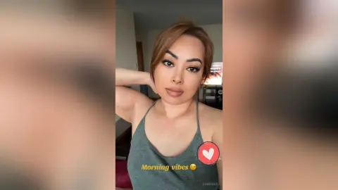 DaniReed poses in a grey tank top, looking at the camera with her hand behind her head.