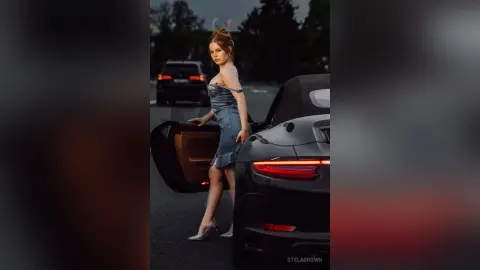 StelaBrown stands next to a black car, wearing a blue denim bustier top and a matching denim skirt.