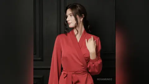 Elegant woman in a red silk robe posing against a dark classic wall for a sophisticated mood.