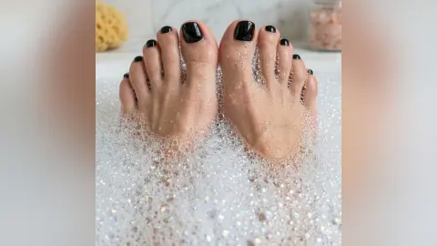 AmberParcker's feet with black nail polish resting in a thick layer of white soap bubbles in a bath.