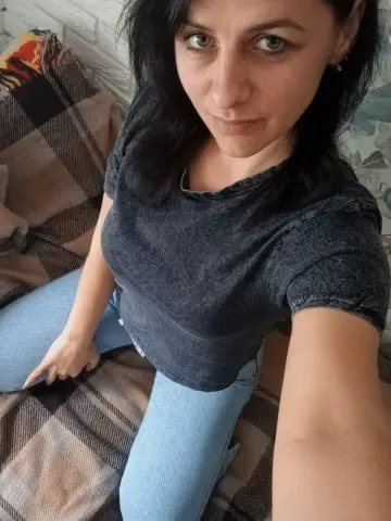 Young woman in a casual dark t-shirt and blue jeans relaxing on a plaid blanket in a cozy indoor setting.