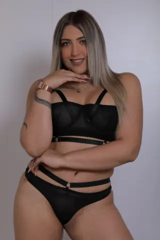Blonde woman in black lace lingerie posing confidently against a plain white studio background.