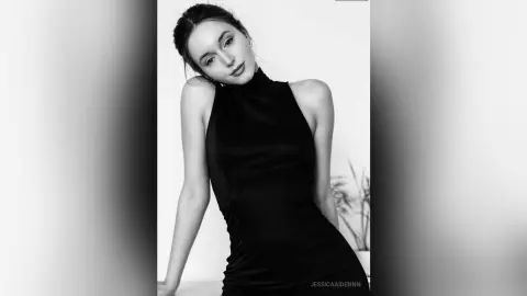 JessicaAidennn — Elegant woman in a sleek black halter neck dress posing against a minimalist white background in black and white.