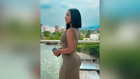 Stylish woman in a tight olive green dress standing on a city balcony overlooking a skyline at dusk.