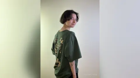 Smiling young woman in an oversized green graphic t-shirt posing in a minimalist indoor setting.