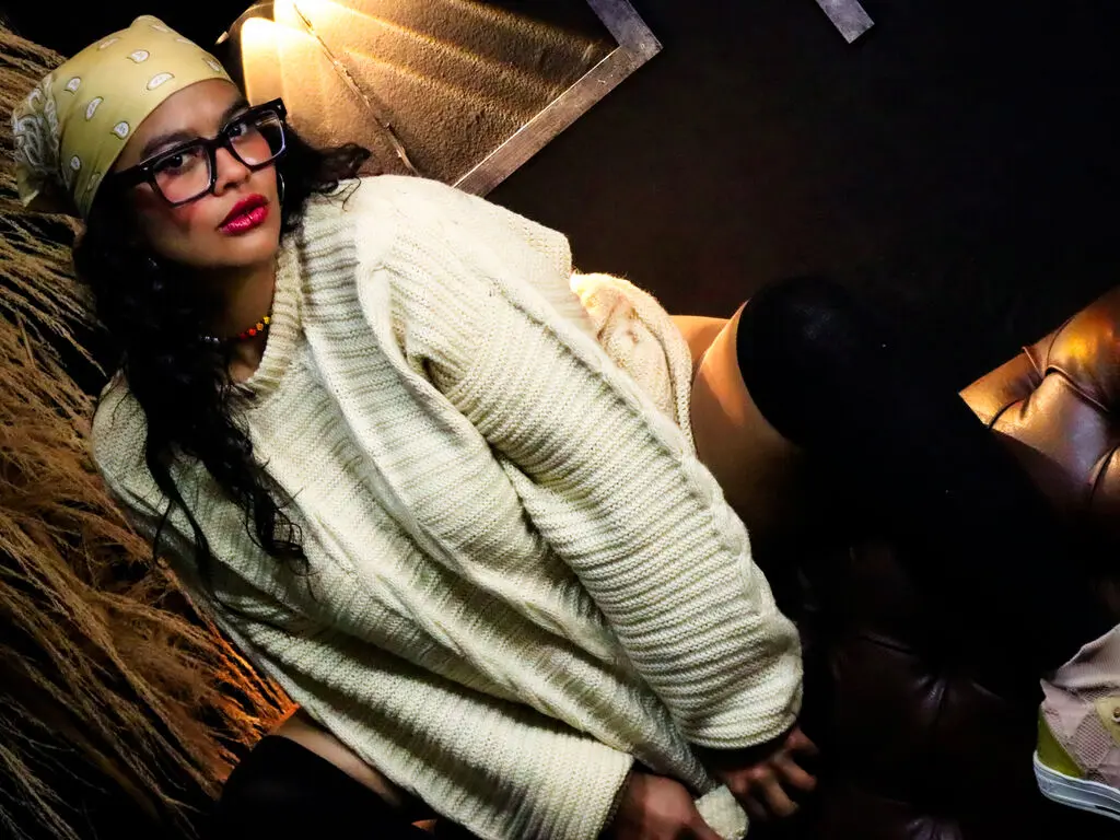 Woman in a cream ribbed sweater and yellow headscarf relaxing on a dark leather sofa in moody lighting.