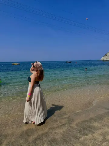 Young woman in a white maxi skirt and bikini top enjoying a sunny day at a tropical beach.