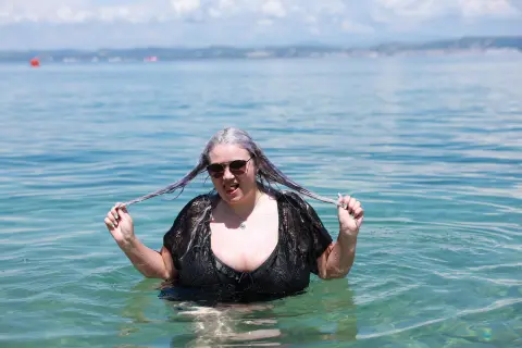 Smiling woman in a black swimsuit playing with her hair in clear turquoise ocean water on a sunny day.